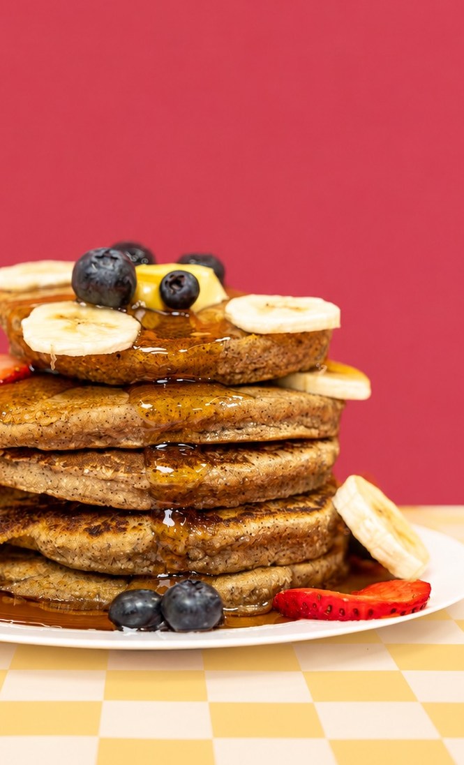 A tall stack of Sol Food pancakes topped with bananas, blueberries and syrup
