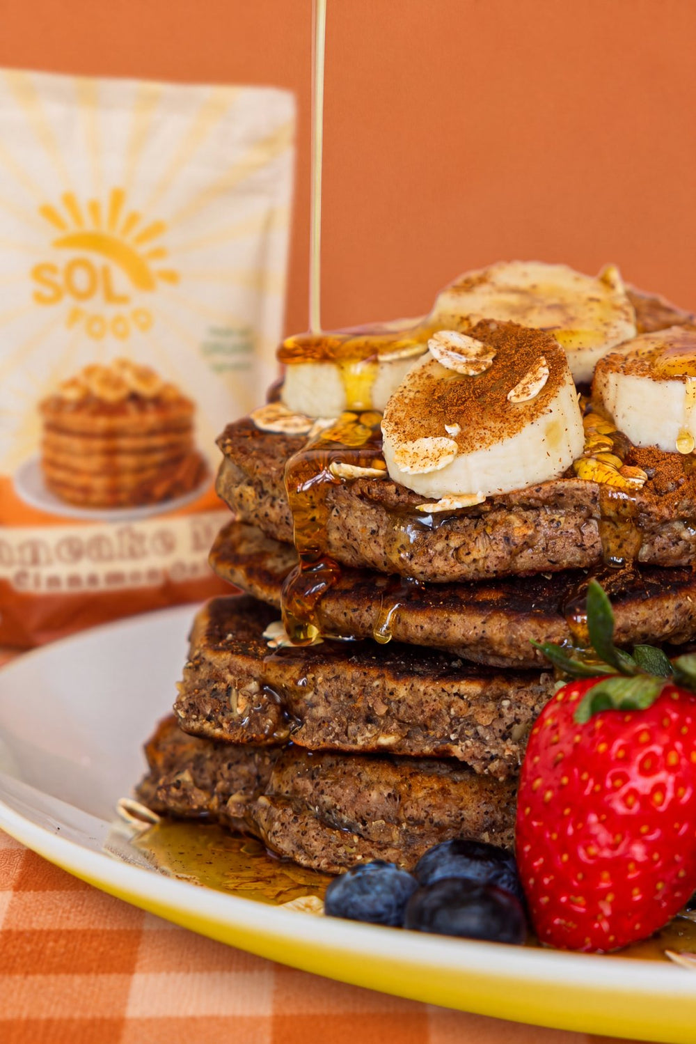 Cinnamon oat pancakes with syrup, banana and berries beside a bag of the mix