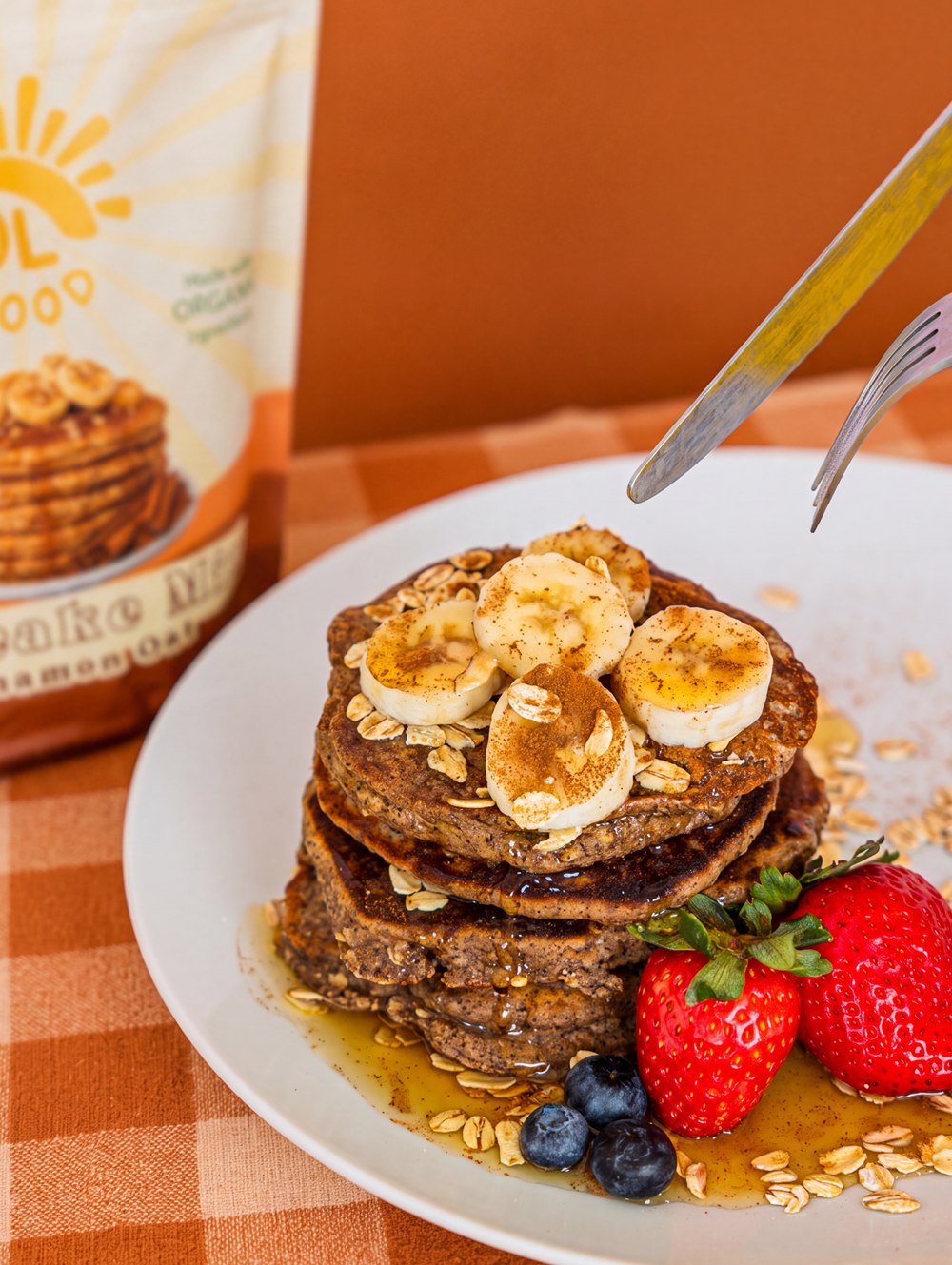 Cinnamon oat pancakes with banana, oats, strawberries and syrup beside a bag of Sol Food mix